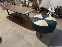 Photo showing the full coffee table and the vinyl ottoman placed on concrete floor with shoes and other items in background.