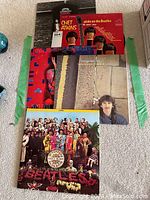 Five vinyl records arranged on carpet: Sgt. Pepper's Lonely Hearts Club Band, solo albums from Beatles members John Lennon, Paul McCartney, George Harrison, and Chet Atkins tribute album.