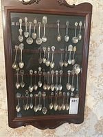 Full view of the wooden wall-mounted display rack showcasing four rows of collector spoons with varied detailed handles.