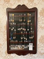 Full view of wooden wall display rack with glass front showing all spoons inside