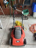 Front view of the Black & Decker electric lawnmower showing the orange deck, black bumper, wheels, and brand label.