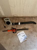 Electric blower and hedge trimmer laid on ground with blower manual present.