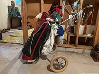 Golf bag loaded with golf clubs and attached to a two-wheeled golf cart. Visible knit head covers on some clubs and hanging golf towels.