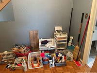 Wide shot showing multiple household items including broom, storage unit, cleaning products, hangers, shoe rack, dish rack, bucket and cords