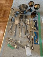 Overview of lot items displaying sterling silver fork and spoon, silver plated goblets, serving utensils, collector spoons and other pieces.