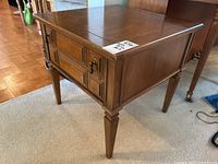 Side angle view showing the single drawer with decorative knob, wood veneer finish, and tapered legs with carved accents.