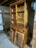 Full view of pine wood cabinet showing natural finish, upper shelves with framed doors, two drawers, and lower storage with transparent doors slightly open.