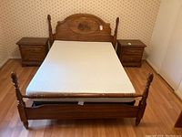 Front view of oak queen bed showing poster headboard with covered bridge carving, mattress, footboard and side railings.