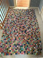 Full view of colorful handmade yo-yo quilt spread on floor showing numerous fabric rosettes in a patchwork style.