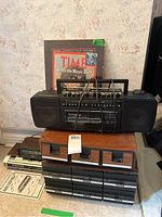 Full view of the retro lot showing Magnavox portable dual cassette tape deck radios, alarm clock radios, cassette tape holders with tapes, and framed Time Magazine print.