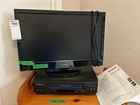 Black Sanyo 22 inch LED-LCD TV with Panasonic VHS player underneath on wooden surface, TV power cord wrapped on side, no remote control visible.
