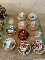 Nine assorted vintage teacups and saucers arranged on carpet, various floral patterns visible, includes one extra cup without saucer.