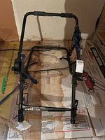 Full view of Thule bike carrier frame showing main structure, straps, and attachment arms on a cardboard surface.