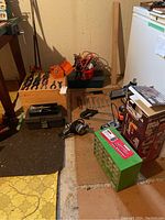 View of assorted wrenches, tools, drill press stand, boxed hardware caddy, clamps, rope, and saw arranged on floor.
