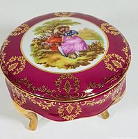 Angled view of the jar showing the Fragonard Love Story painting on top with gold decoration and three gold legs.