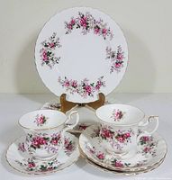 Photo showing two demitasse cups with matching saucers and one lunch plate displayed upright, highlighting lavender rose floral pattern and gold trimmed edges.