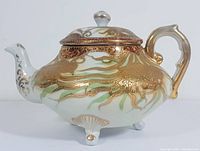 Front right side view of the vintage teapot showing heavy gold moriage design with green accents, white porcelain base, and silver knob on the lid.
