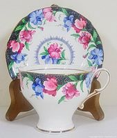 Photo showing front view of footed tea cup with pink and blue flowers and saucer with matching floral design on display stand.