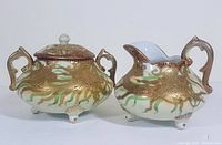 Side view of creamer and sugar bowl showing detailed gold encrusted floral patterns and ornate handles.