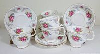 Set of six white fine bone china tea cups stacked with six matching saucers showing pink rose floral and blue flower pattern with silver-gray scroll and gold trim.