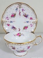 Front angled view of teacup with saucer in background showing floral detailing and gold trim on white bone china.