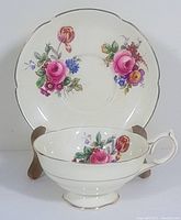 Teacup and saucer set with floral pattern and gold trim displayed on wooden stand.