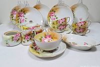 Full view of Nippon set showing teacups, plates, mint dishes, and sugar containers adorned with hand-painted pink roses on white and yellow background.