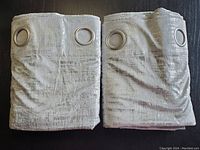 Two soft velvet curtain panels folded with metal grommets visible, showing champagne color with silver print.