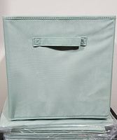 Front view of one foldable fabric basket bin in light blue/grey color showing rectangular stitched handle.
