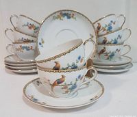 Eight teacups stacked and arranged with their matching saucers behind, showing the hand-painted Golden Pheasant and floral pattern with gold trims.