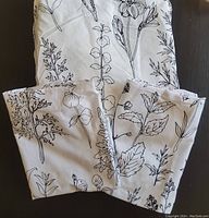 Folded duvet cover and two pillowcases showing botanical pattern on white fabric.