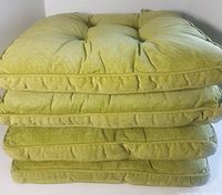 Stack of four new green corduroy tufted chair cushions showing thickness and fabric texture.