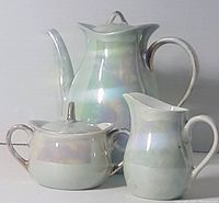 Photo showing the full three-piece tea set including tea pot, sugar bowl with lid, and creamer, all in iridescent lustreware finish.