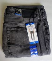 Front view of folded black denim jeans showing back pocket, size tags, and Buffalo David Bitton label tags attached