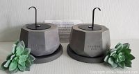 Pair of gray geometric concrete tabletop fire pits with metal lids and bases, displayed with faux succulent plants and instruction manual.