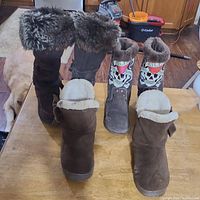 Photo showing three pairs of boots from front angle: black tall boots with faux fur, brown suede boots with fleece, and gray Ed Hardy boots with skull and heart design.