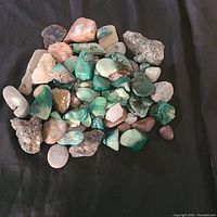 Top view of mixed chrysocolla, quartz, amber, and other mineral stones on black cloth backdrop.