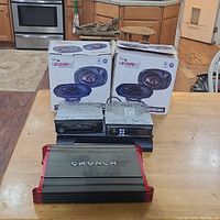 Photo showing all items on a wooden table: Crunch amplifier, Phoenix Gold amplifier, Sony and Alpine stereos, and two boxes of car speakers