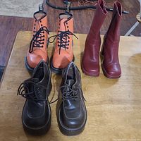 Photo of all three pairs of boots and shoes on wooden table: tan Dr. Martin Air Wairs, dark brown splash shoes, and red vintage boots.