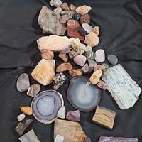 Top view of assorted geode and mineral specimens showing polished geode slices, rose quartz, and petrified wood pieces spread on black fabric.