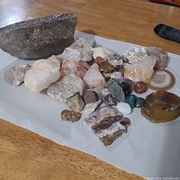 Top-down view of assorted geological specimens including rough and polished crystals and stones grouped on a wooden surface with white backing sheet.