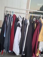 Rack of men's clothes showing jackets and hoodies in various colors hanging on a rack outdoors with a window and sky in background.