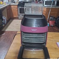 Front view of Power Air Fryer Oven showing open front door, four metal baking trays inside, and removable mesh basket on top.
