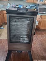 Front view of the large stainless steel electric smoker with glass door, showing racks inside and control panel on top.