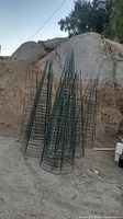 Photo showing six tall green metal vegetable cages outdoors, conical in shape, set against natural rocky background.