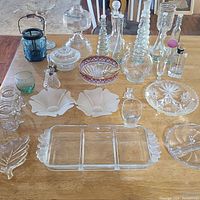 Photo of assorted vintage glass bottles, dishes, and decorative items arranged on a wooden table.