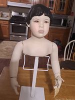 Full view of the vintage boy doll head and upper torso bust mounted on a white metal stand, showing the detailed facial painting and articulated arms.