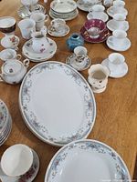 Top view photo showing assorted vintage china pieces including Gibson bowls, platters, cups, and saucers with floral patterns and gold trim arranged on a wooden table.
