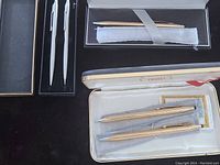Two vintage Cross pen sets: one gold-tone ballpoint pen with matching mechanical pencil in cream box, and two white pens in black box.