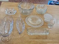 Top-down view showing all the clear glass and crystal bowls and dishes arranged together on a wood surface. Items include mixing bowls, divided candy dishes, decorative plates, and a small drinking glass.